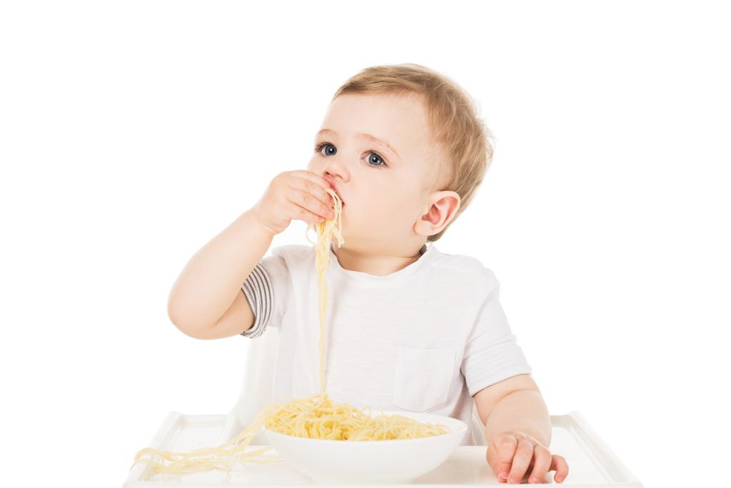 Kleiner Junge im Hochstuhl isst Spaghetti von Hand isoliert auf weißem Hintergrund  - Foto, Bild