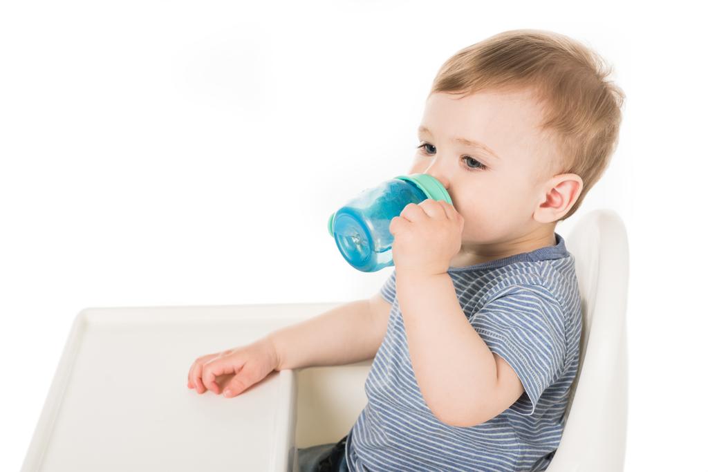  赤ちゃんカップと白い背景で隔離のハイチェアに座っているからの小さな少年の飲料水  - 写真・画像