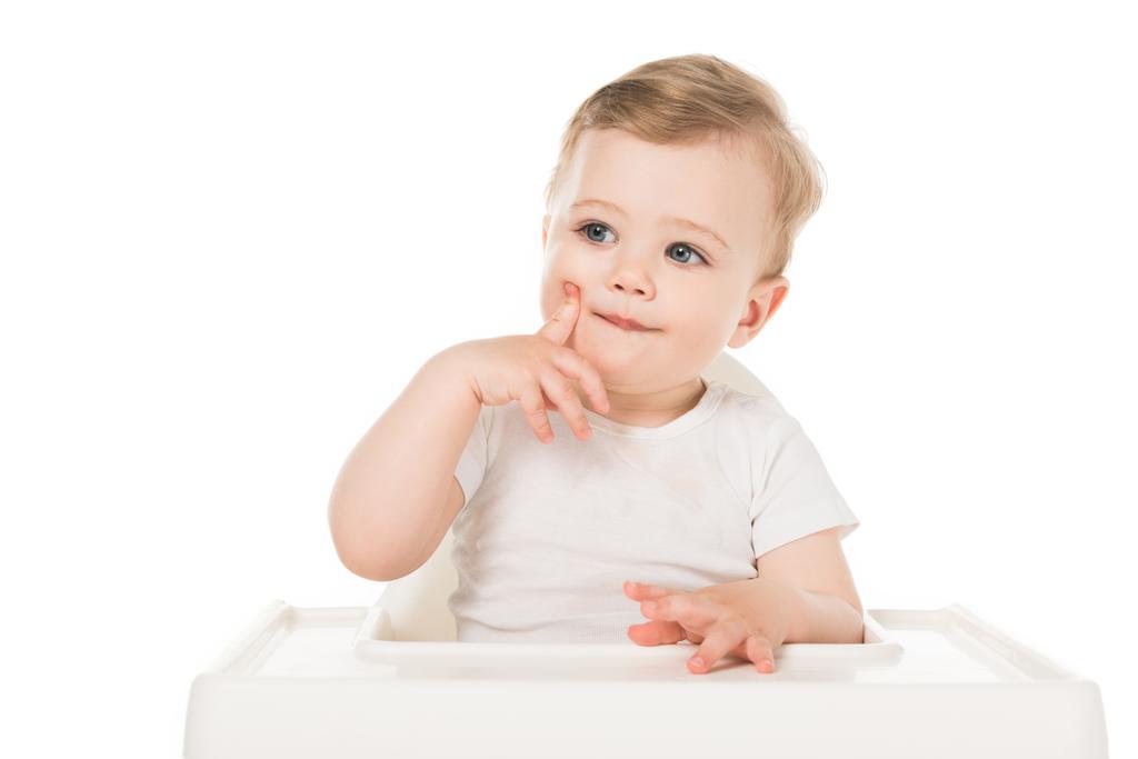 αξιολάτρευτο μικρό αγόρι κάθεται σε καρεκλάκι που απομονώνονται σε λευκό φόντο  - Φωτογραφία, εικόνα