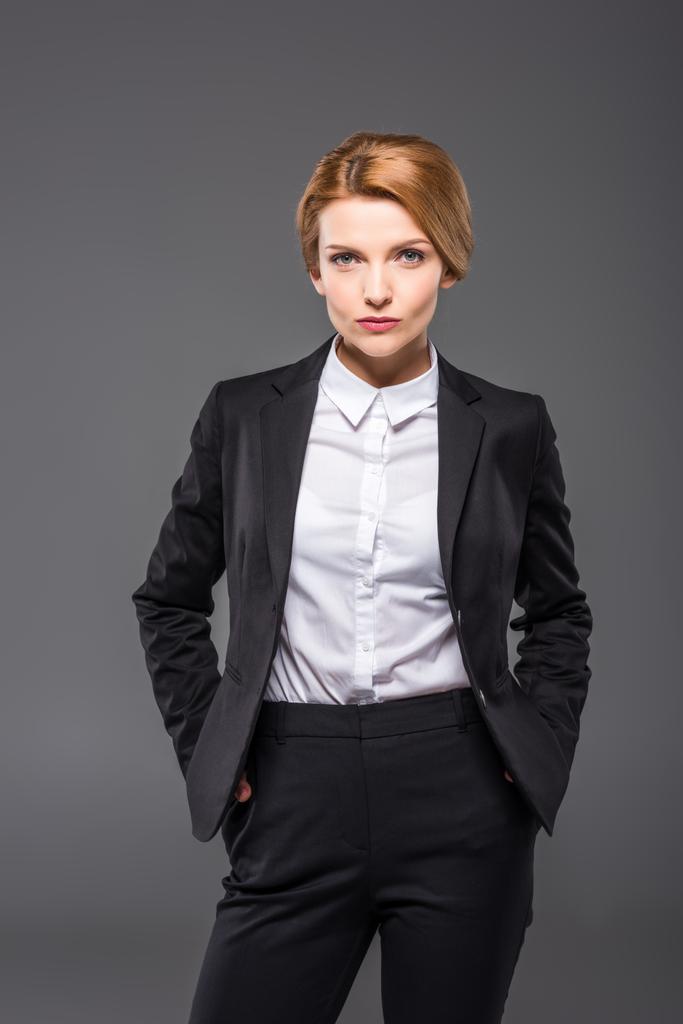 Selbstbewusste Geschäftsfrau posiert im Anzug mit den Händen in den Taschen, isoliert auf grau - Foto, Bild