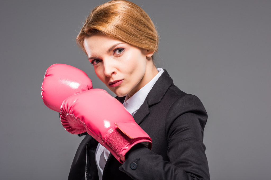 портрет серьезной предпринимательницы, позирующей в розовых боксерских перчатках, изолированных на сером
 - Фото, изображение