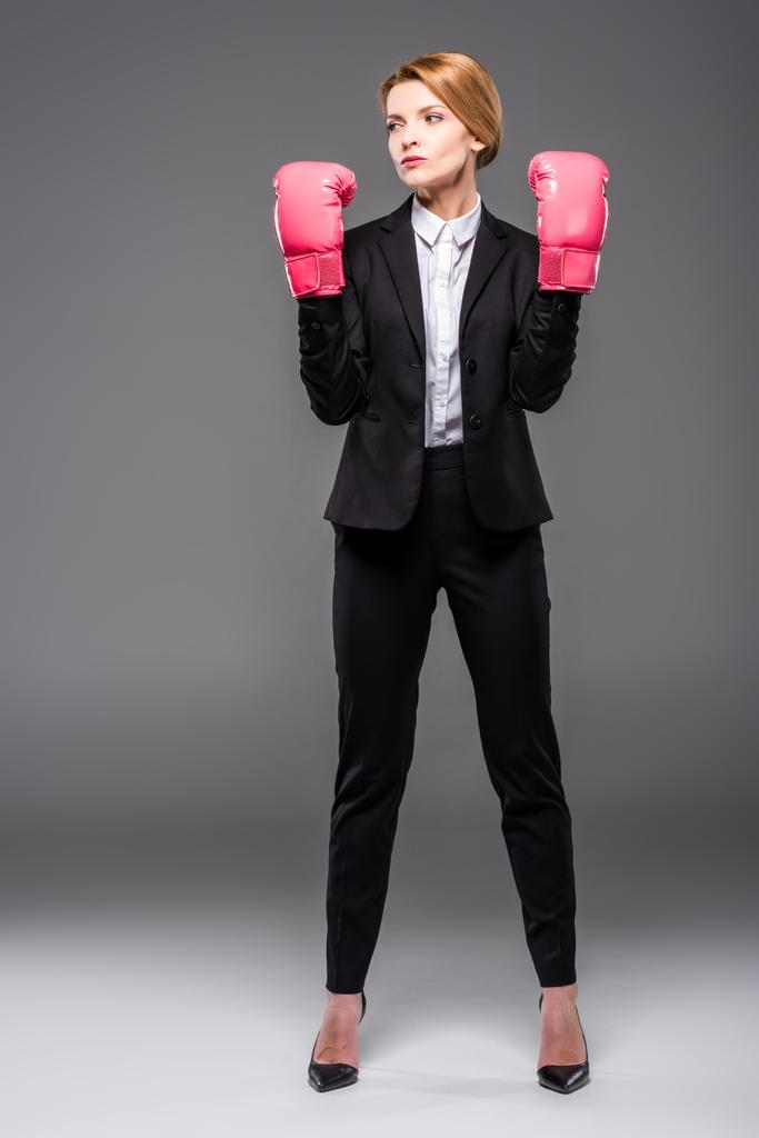 confident businesswoman posing in suit and pink boxing gloves, isolated on grey - Photo, Image