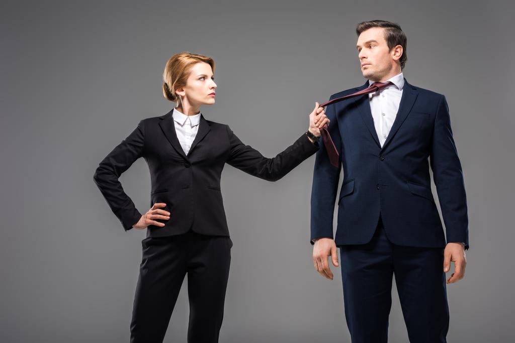 aggressive businesswoman holding tie of businessman, isolated on grey - Photo, Image