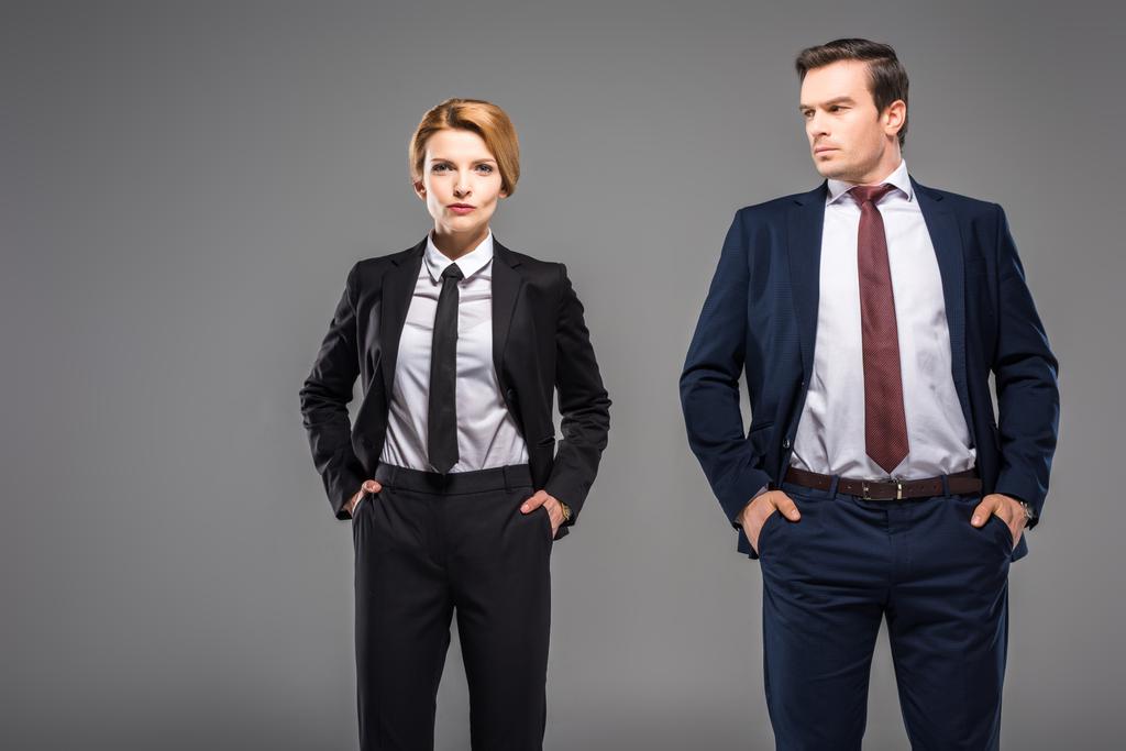 seriöse Geschäftsfrau und Geschäftsmann posiert mit den Händen in den Taschen, isoliert auf grau - Foto, Bild