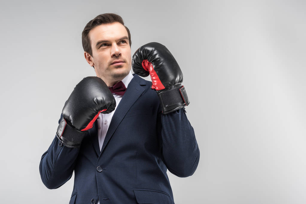 handsome thoughtful man in suit and bow tie wearing boxing gloves, isolated on grey - Photo, Image