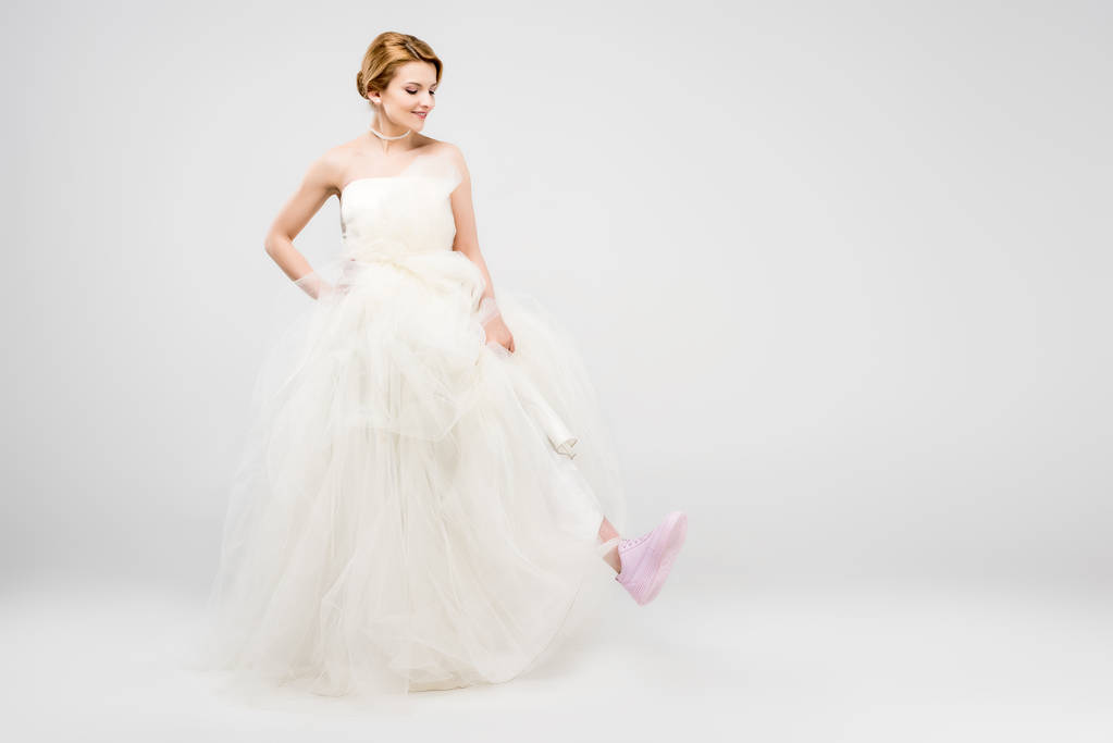 白いウェディング ドレスとピンクのスニーカー、灰色、フェミニズムの概念に分離された陽気な花嫁 - 写真・画像