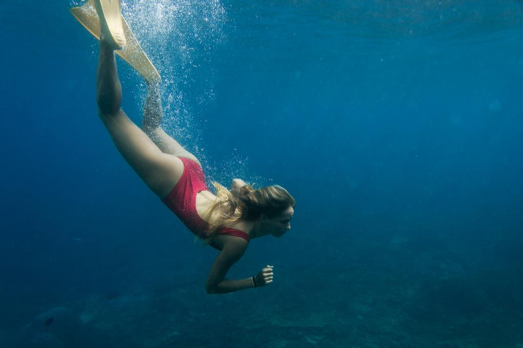 underwater photo of young woman in swimming suit and fins diving in ocean alone - Photo, Image