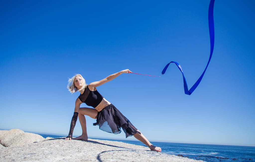 Beautiful fitness model doing ribbon dancing on granite rock overlooking ocean on bright and sunny summer day - Photo, Image