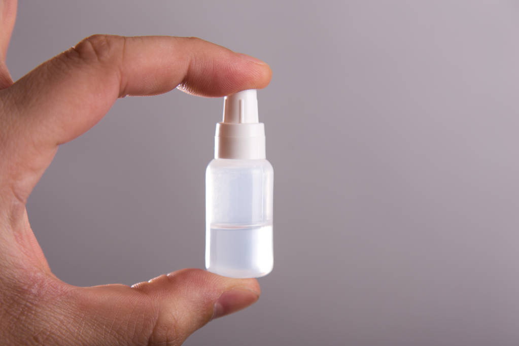 A small tube with a colorless liquid in a hand on a gray background - Photo, Image