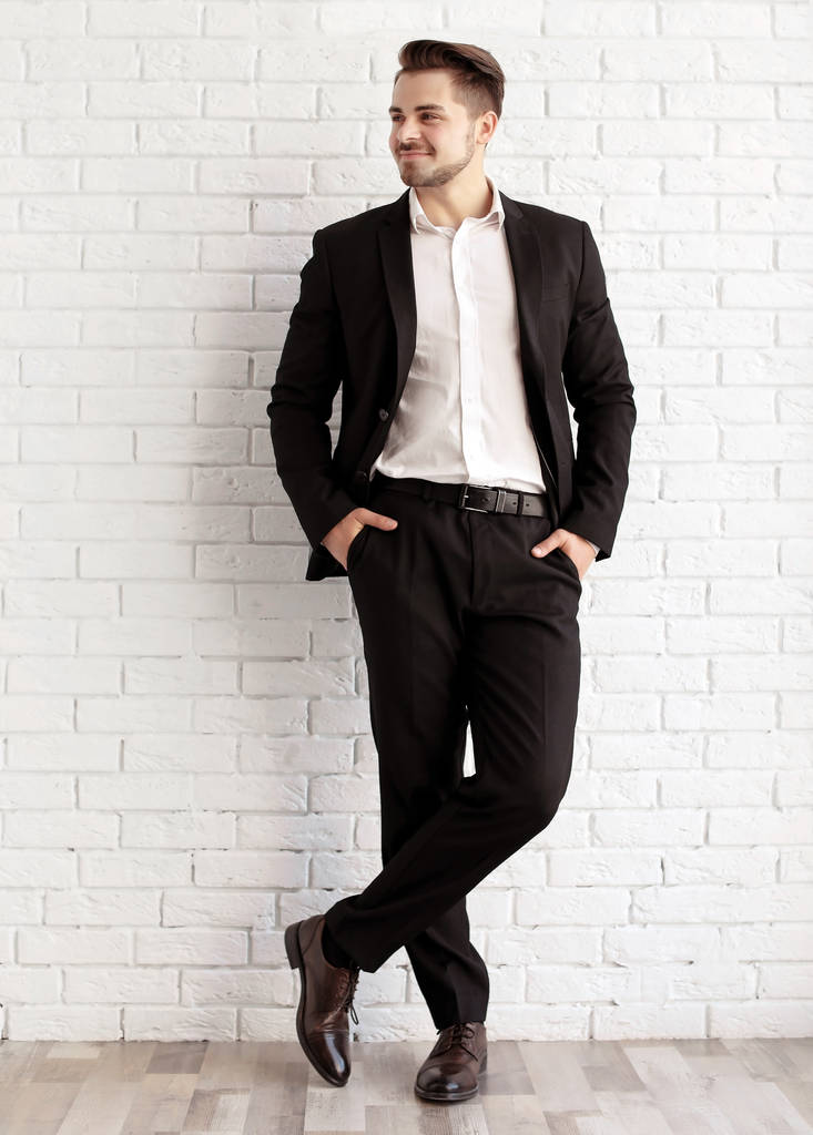 Όμορφος νεαρός άνδρας στο κομψό κοστούμι και παπούτσια δερμάτινα κοντά σε τοίχο από τούβλα - Φωτογραφία, εικόνα