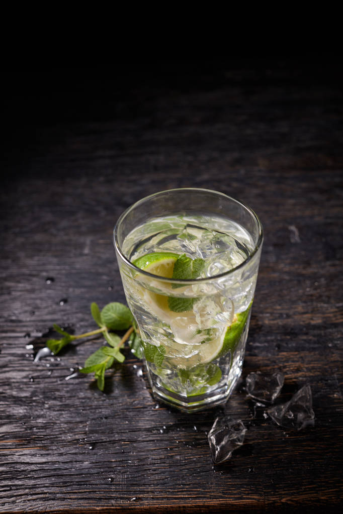 Ποτήρι παγωμένο κοκτέιλ μοχίτο και συστατικά, ασβέστη, πάγο και μέντα φύλλα σε μαύρο φόντο, ποτό κρύο το καλοκαίρι  - Φωτογραφία, εικόνα