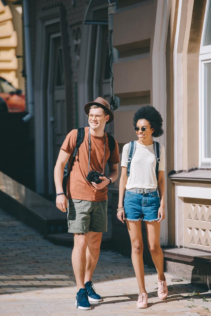 interracial couple of young tourists with camera walking on street - Photo, Image