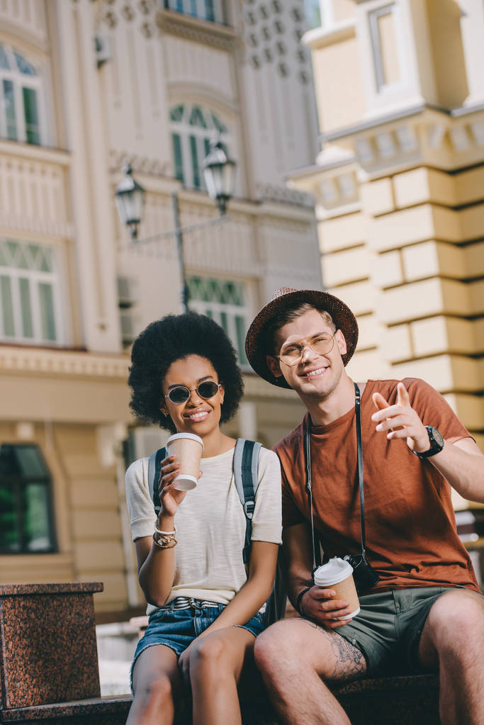 viaggiatore maschio sorridente che punta il dito alla fidanzata afro-americana con tazza di carta di caffè
  - Foto, immagini