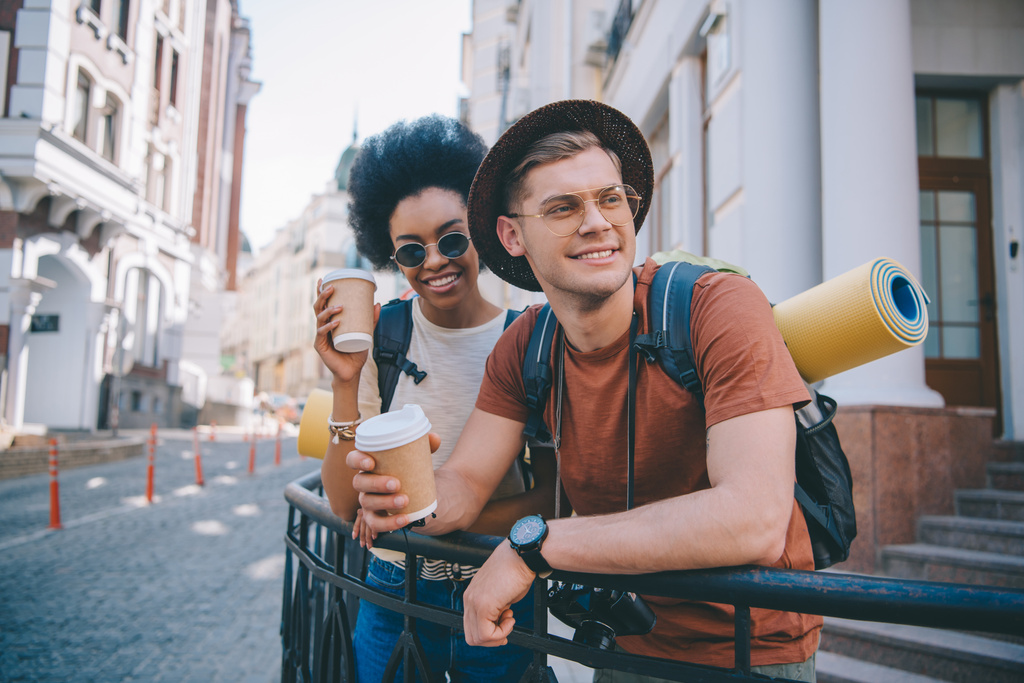 sorridente coppia multiculturale di turisti in piedi con tazze di caffè usa e getta
  - Foto, immagini
