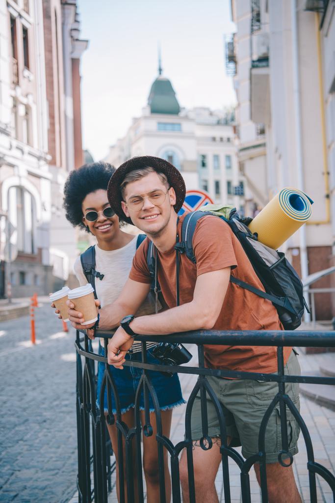happy young interracial couple of travelers with paper cups of coffee - Photo, Image