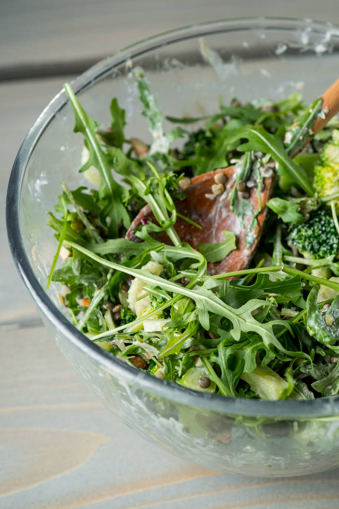 foto de cerca de la deliciosa ensalada verde con rúcula y espinacas en un tazón de vidrio con cuchara de madera en la mesa
  - Foto, Imagen