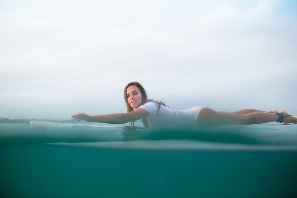 attractive sportswoman in white swimsuit swimming on surfboard in ocean - Photo, Image