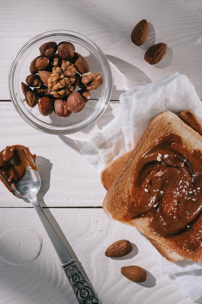 白い木製のテーブルの上とボウルにチョコレートと異なるナッツ食パンのトップ ビュー - 写真・画像
