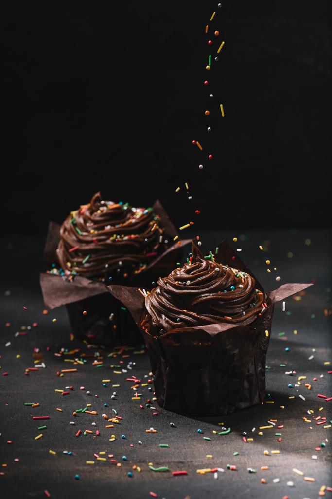 Sabrosos cupcakes de chocolate con crema y azúcar extendiéndose sobre la mesa
 - Foto, Imagen