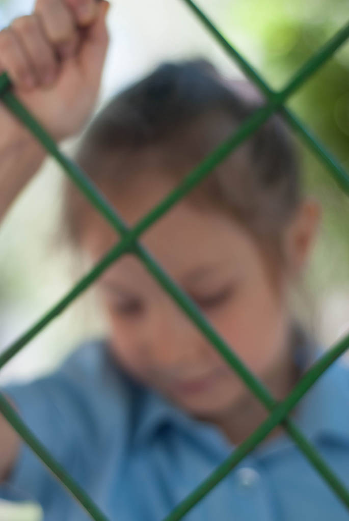 Mädchen hinter Gittern. Trauriges blaues Schulmädchen hinter Gittern. Kindererziehung, Bildung. - Foto, Bild