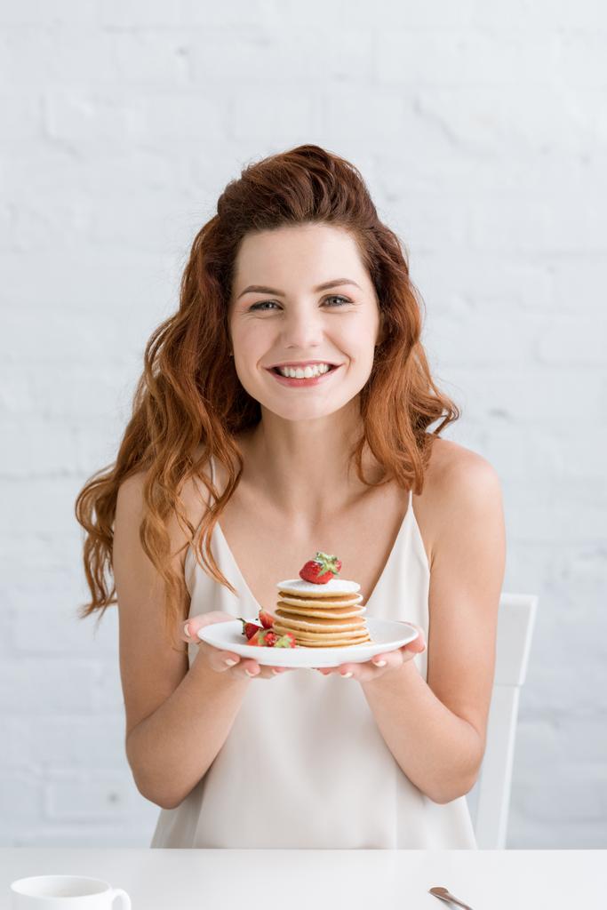 красивая молодая женщина держит вкусные блины на тарелке и смотрит в камеру
 - Фото, изображение