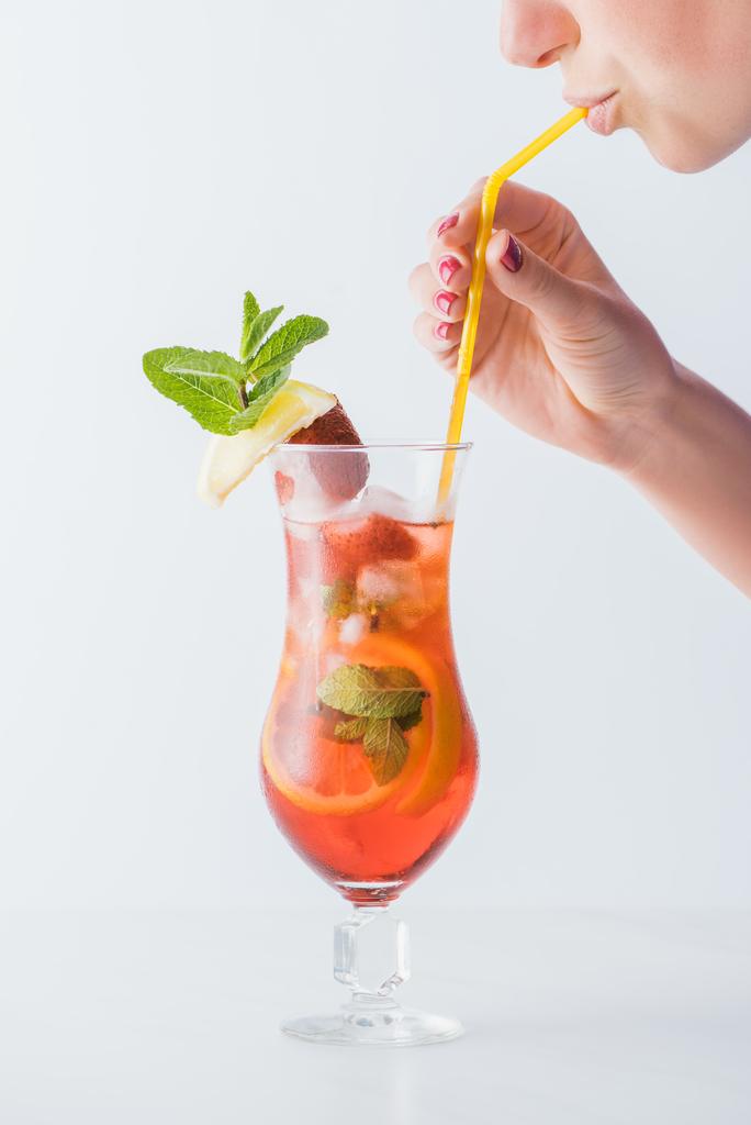 Teilansicht einer Frau, die einen sommerlichen kalten Cocktail mit Zitrusfrüchten, Erdbeere und Minze trinkt, isoliert auf weiß - Foto, Bild