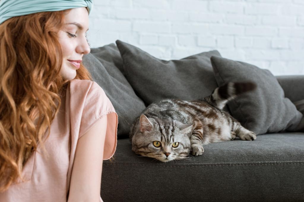 attractive young woman smiling at adorable tabby cat at home - Photo, Image