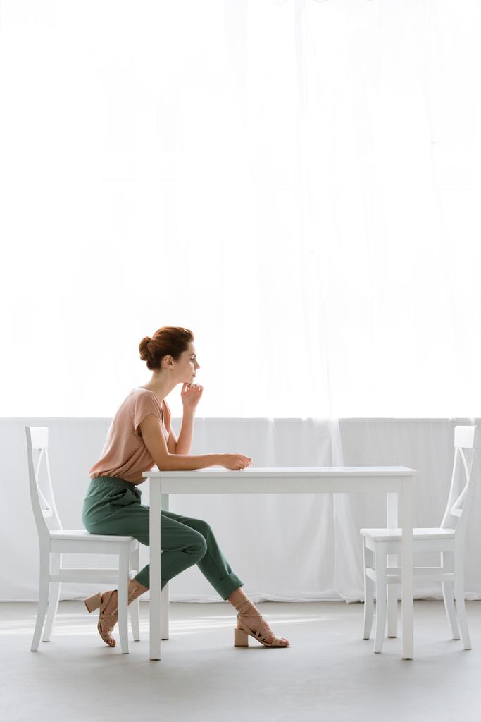 Widok z boku z piękną, młodą kobietę, siedzi przy stole w domu - Zdjęcie, obraz