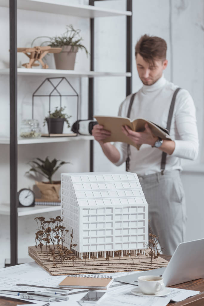 επιλεκτική εστίαση του αρχιτέκτονα διαβάζοντας το περιοδικό και το μοντέλο του κτιρίου στο χώρο εργασίας στο γραφείο - Φωτογραφία, εικόνα