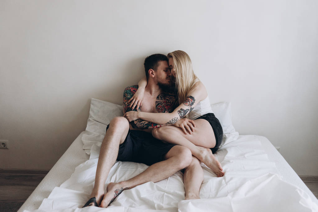Jeune couple tatoué embrassant sensuellement sur le lit à la maison
 - Photo, image