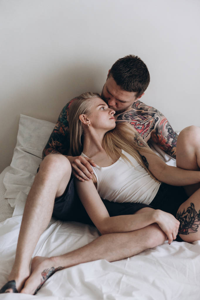 Chica rubia apoyada en sensual hombre tatuado en la cama
 - Foto, Imagen