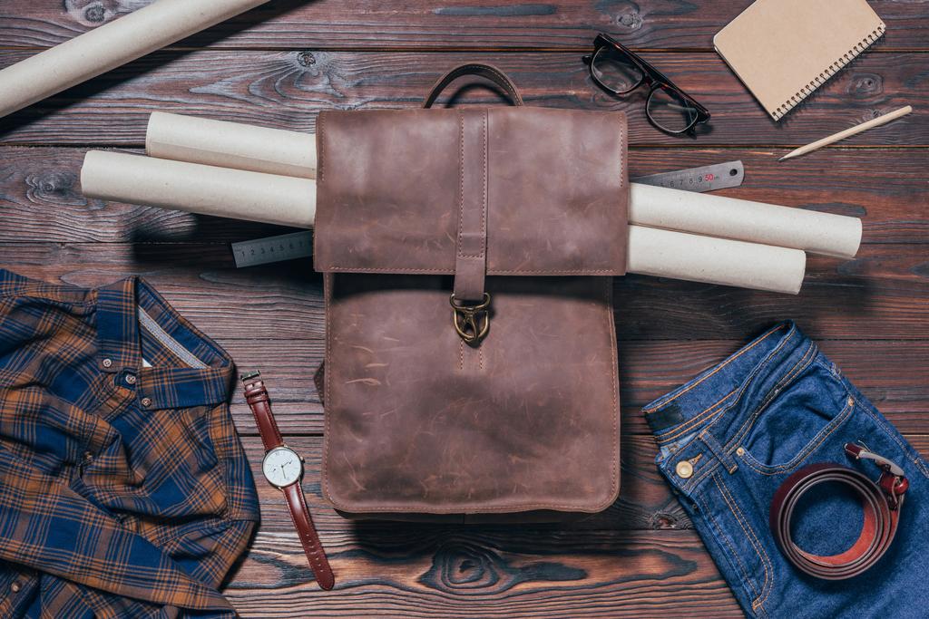 płaskie lay z męskiej koszuli, dżinsy, zegarek i plany w plecaku na drewnianym blatem - Zdjęcie, obraz