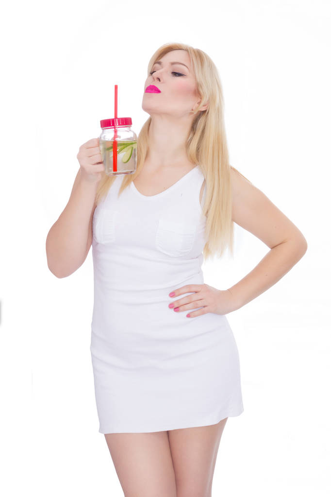 Una mujer rubia y amigable sostiene un vaso de agua y cal en sus manos. Una chica está bebiendo limonada. Concepto - comida saludable, sed que sacia en verano
 - Foto, Imagen