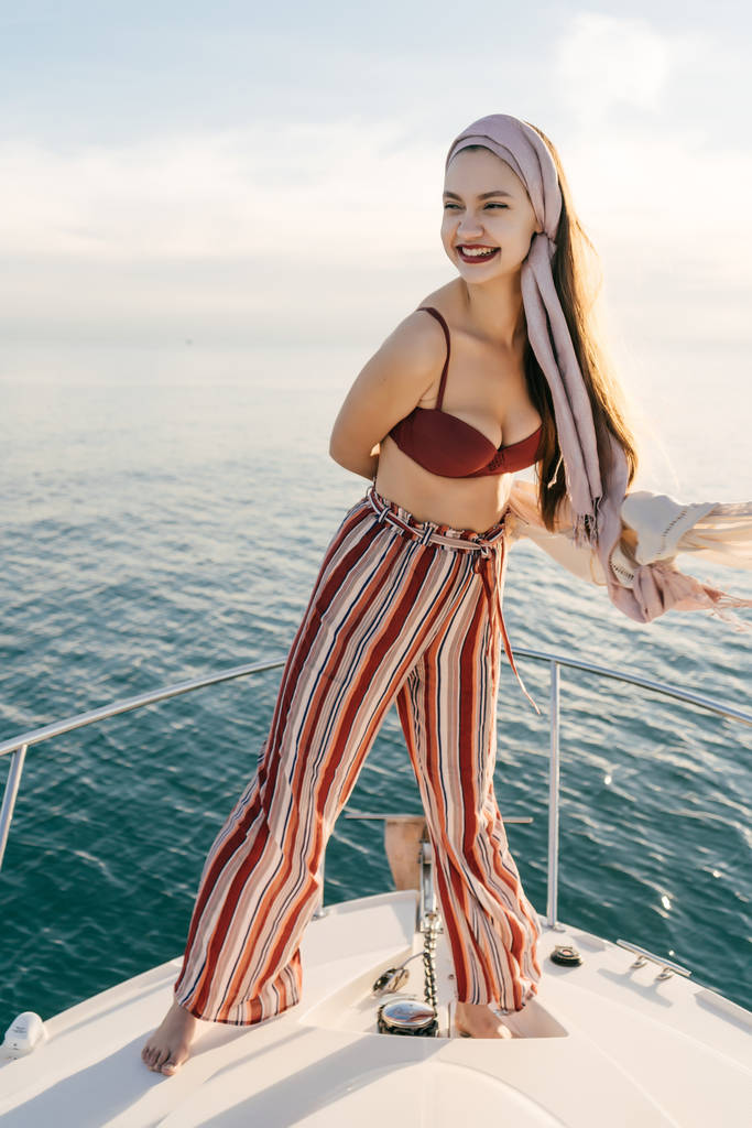 スタイリッシュな夏服の豊富な若い女性は彼女のヨットの上で立ち海の航海を楽しんでいます - 写真・画像