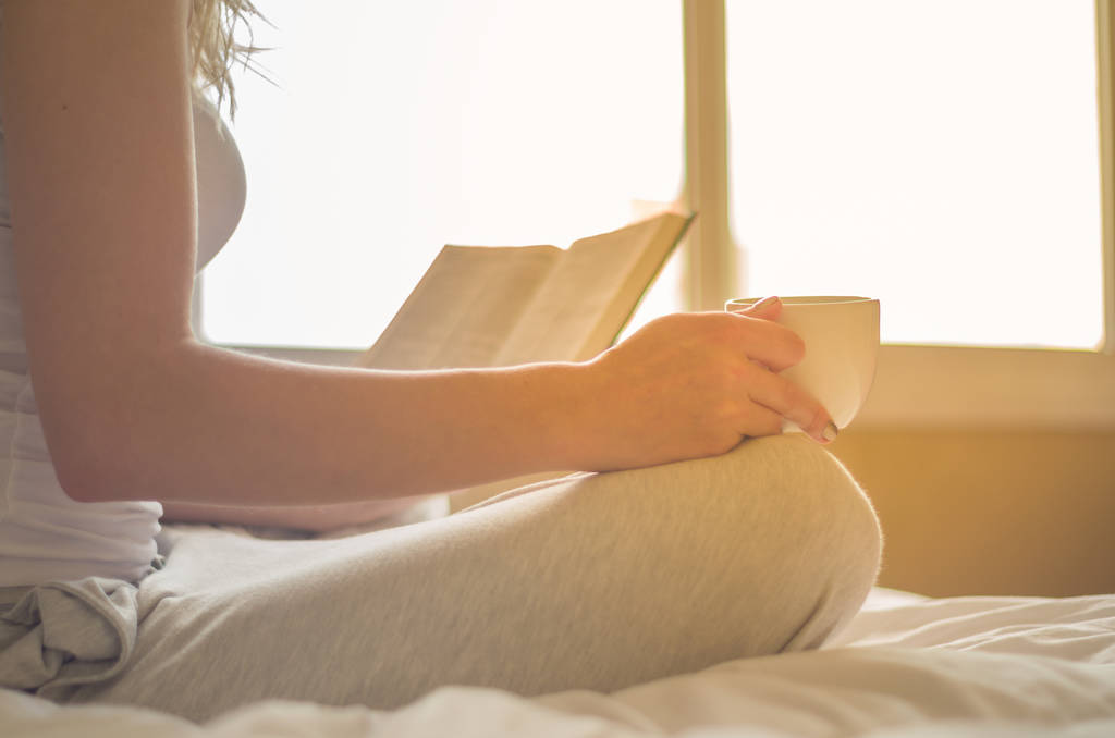 Женщина читает книгу, пить кофе в постели с солнечными лучами в й
 - Фото, изображение