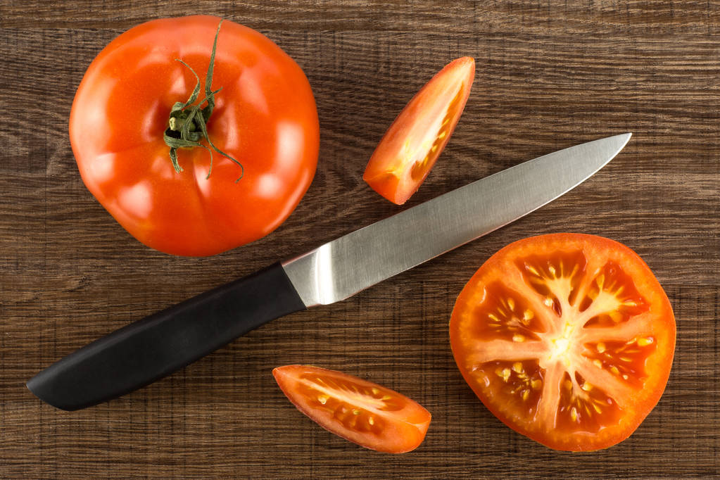 Rode tomaat samenstelling met een mes geïsoleerd op bruin hout achtergrond bovenaanzicht één geheel één sectie helft en twee slice - Foto, afbeelding