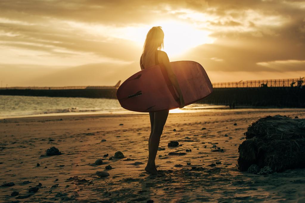 femme surfeuse posant avec planche de surf sur la plage au coucher du soleil avec contre-jour
 - Photo, image