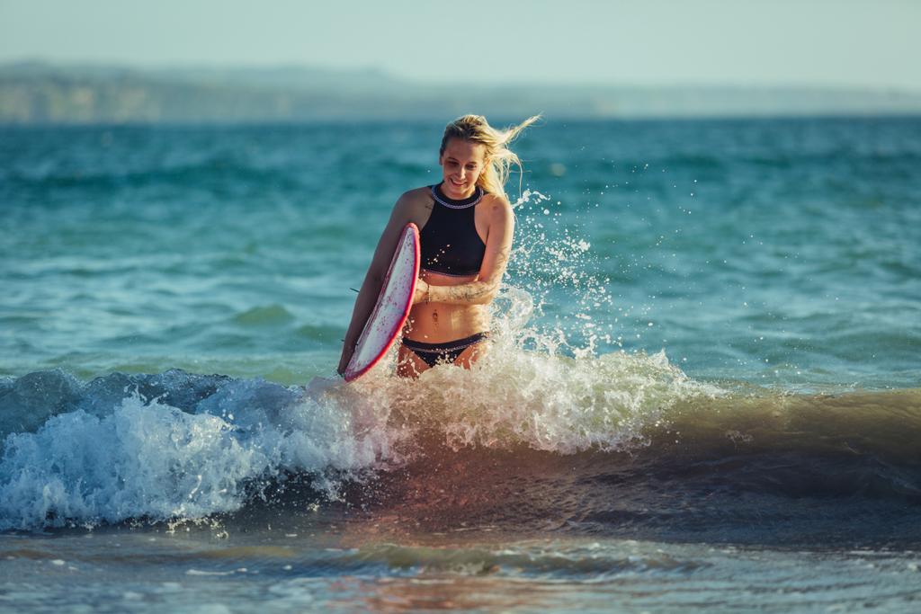 水の中でサーフボードを持つ金髪の女性サーファー  - 写真・画像