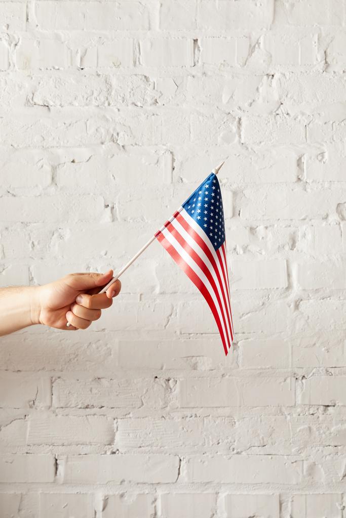 imagem cortada do homem segurando bandeira americana contra parede de tijolo branco
  - Foto, Imagem