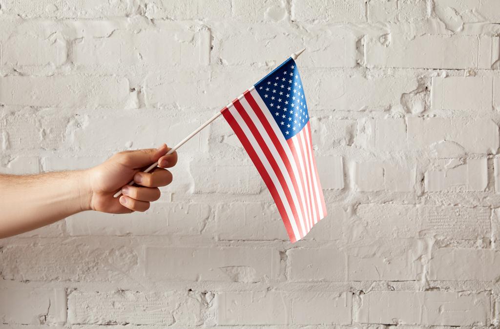 partial view of man holding american flagpole against white brick wall  - Photo, Image