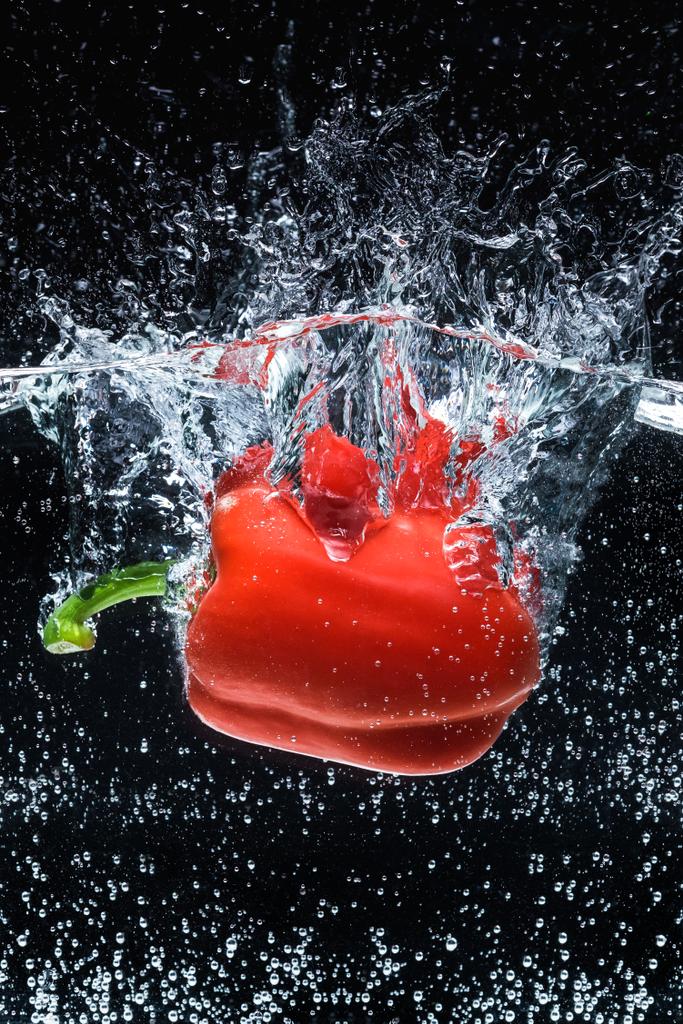 Close-up van rijpe rode paprika in water geïsoleerd op zwart - Foto, afbeelding