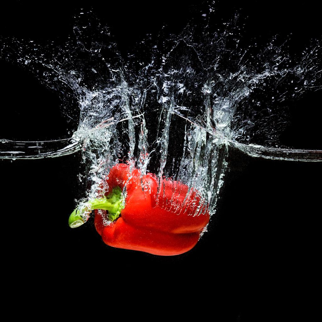 κλείνω πάνω θέα της κίνησης του κόκκινο πιπέρι κουδουνιών, που εμπίπτουν στο νερό που απομονώνονται σε μαύρο - Φωτογραφία, εικόνα
