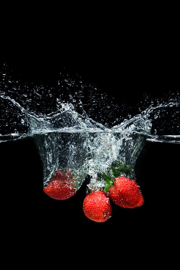 Close-up van de beweging van rijpe aardbeien vallen in water geïsoleerd op zwart - Foto, afbeelding