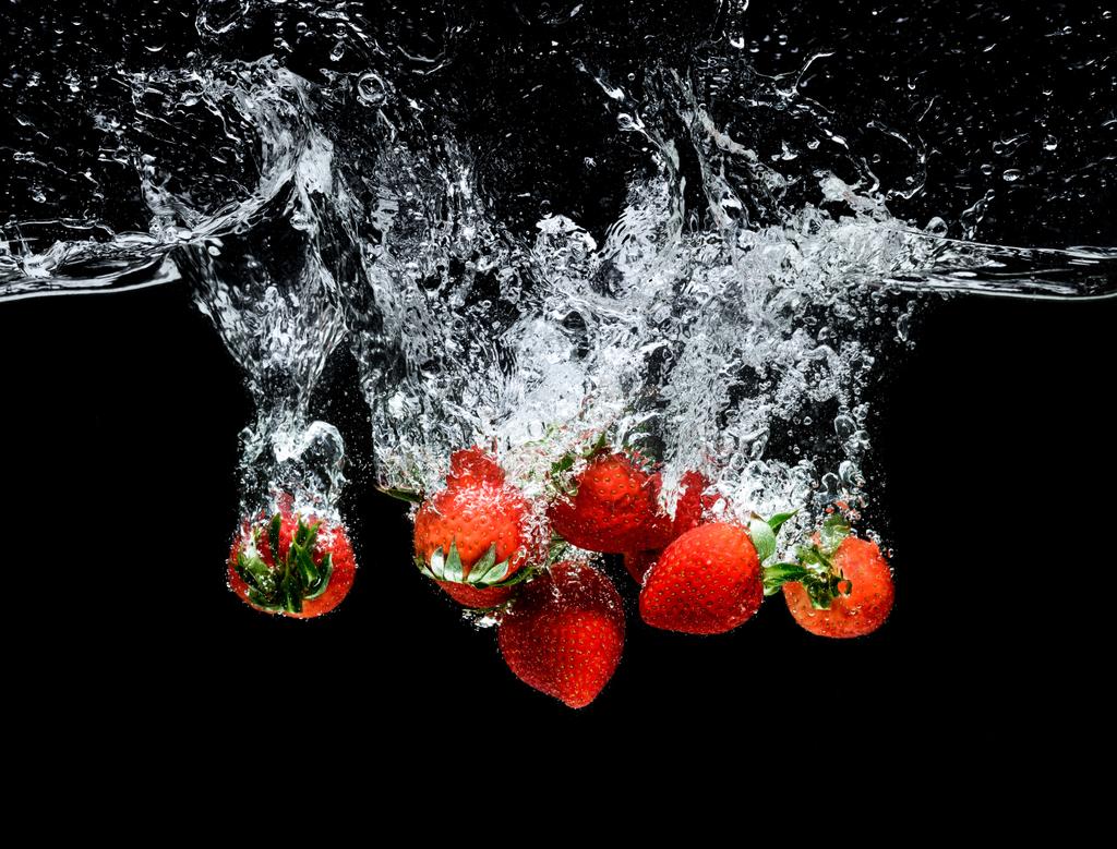 vista de cerca del movimiento de fresas maduras que caen en el agua aisladas en negro
 - Foto, Imagen