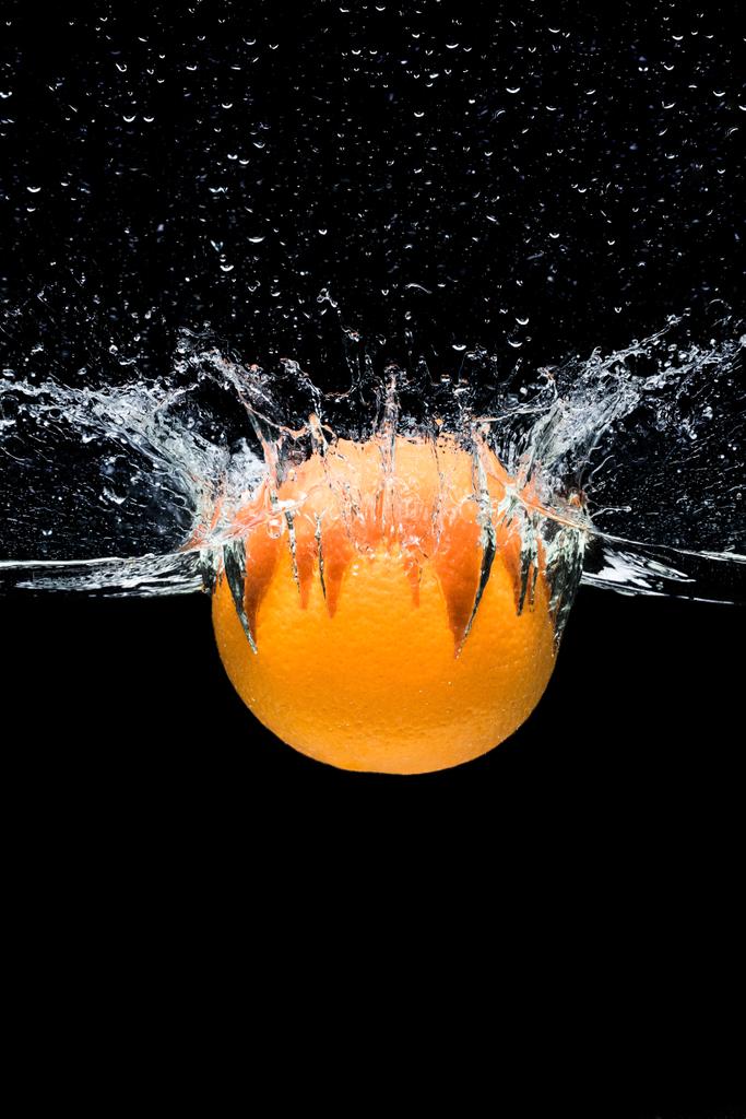 Nahaufnahme von frischen, orangen Zitrusfrüchten, die isoliert auf schwarz ins Wasser fallen - Foto, Bild