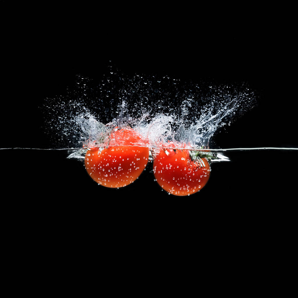 вблизи вид спелых помидоров, падающих в воду изолированных на черном
 - Фото, изображение