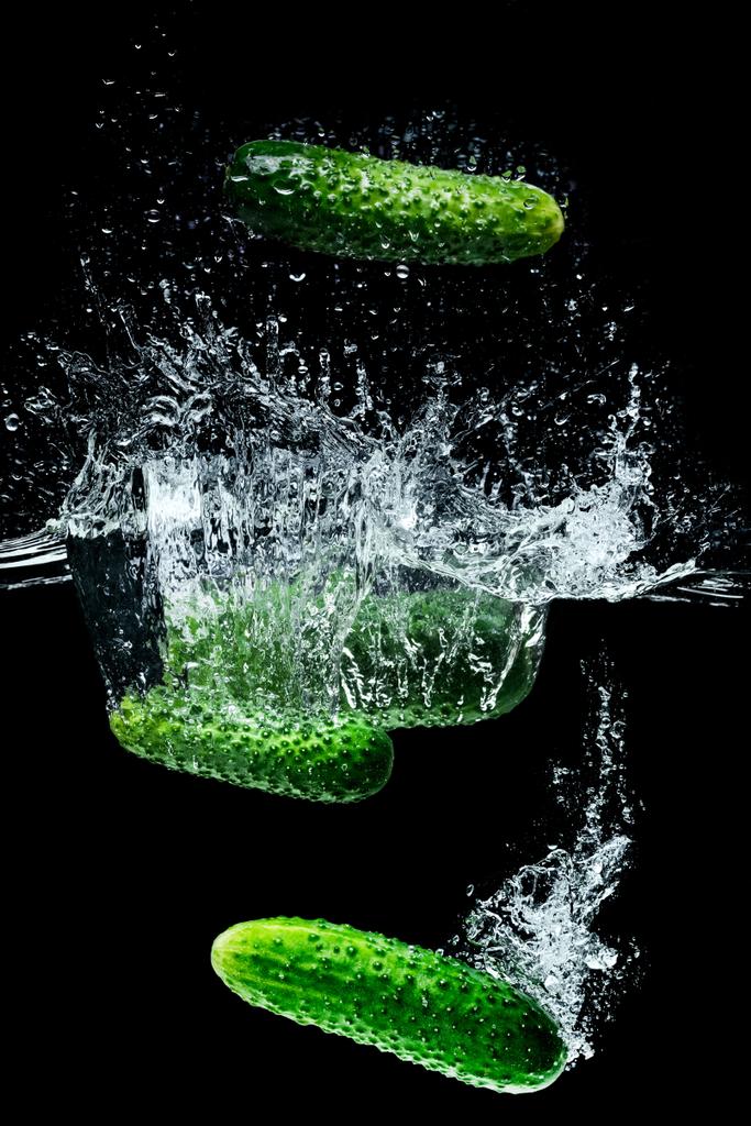 Close-up van rijpe komkommers vallen in water met spatten geïsoleerd op zwart - Foto, afbeelding