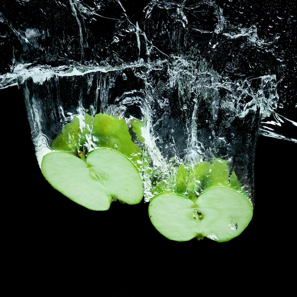 Nahaufnahme von grünen Apfelstücken im Wasser isoliert auf schwarz - Foto, Bild