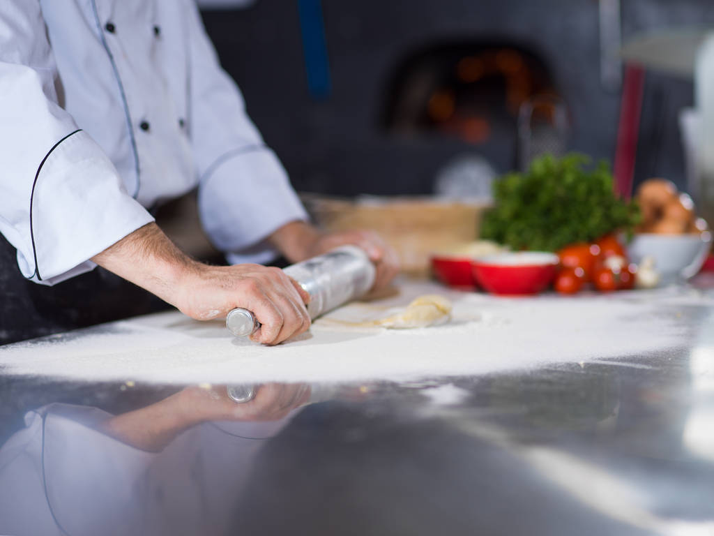 chef preparando la masa para la pizza rodante con rodillo en espolvoreado con mesa de harina - Foto, imagen