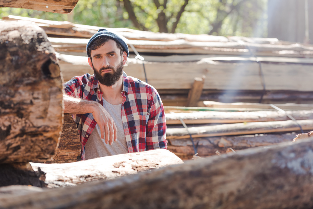 bearded lumberjack in checkered shirt standing at sawmill  - Photo, Image